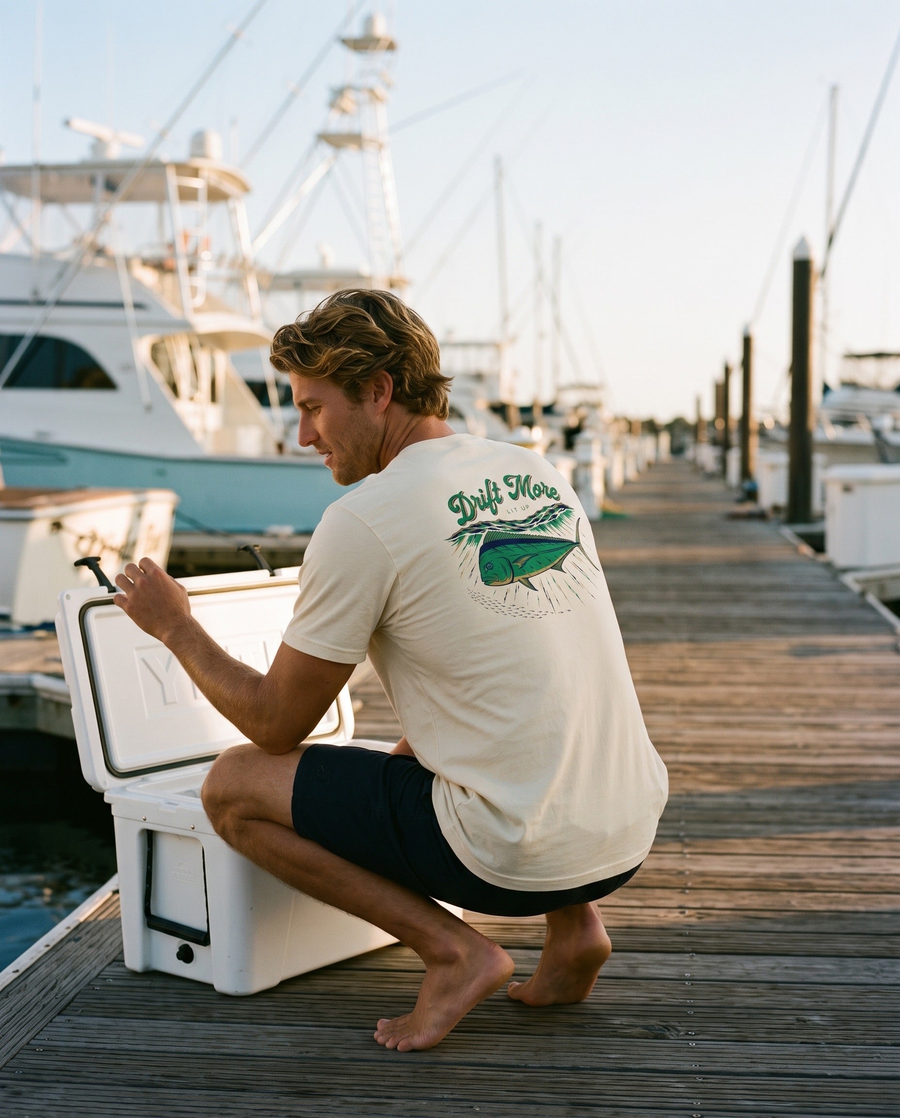 Mahi Lit Up Tee back print, natural cream, crouched on a marina dock